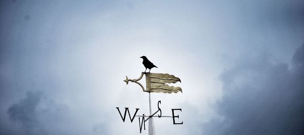 Low angle view of weather vane against clouds