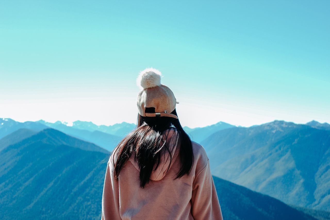 rear view, mountain, sky, real people, beauty in nature, leisure activity, one person, lifestyles, winter, scenics - nature, nature, mountain range, tranquil scene, adult, day, women, clear sky, copy space, holiday, warm clothing, looking at view, hairstyle