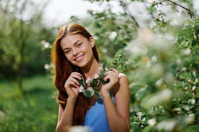 Portrait of young woman drinking water while standing against plants