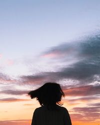 Woman with tousled hair standing against sky during sunset