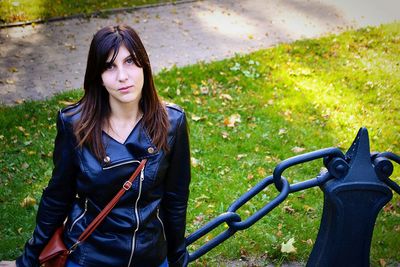 High angle portrait of woman standing by metallic railing on grassy field at park