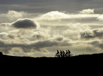 Silhouette people on field against sky during sunset