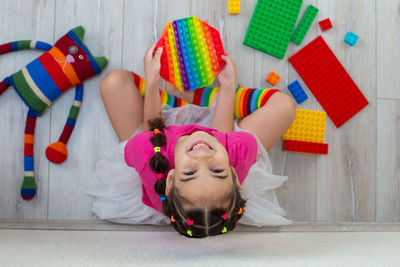 Cheerful little brunette girl in bright colorful clothes, sits on the floor with colorful toys