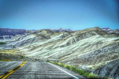 Road leading towards mountains against blue sky