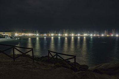 Illuminated city by sea against sky at night