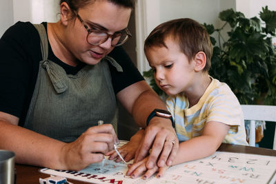 Mom painting her young son's finger nails at dining table