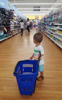Full length of boy with blue bucket standing on hardwood floor in supermarket