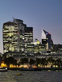 Illuminated buildings by river against sky in city