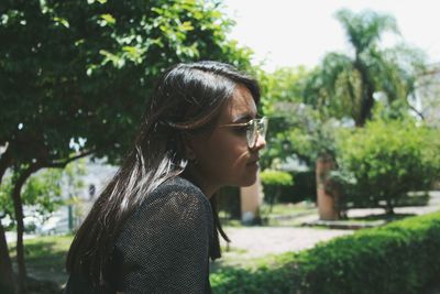 Young woman looking away while standing against trees