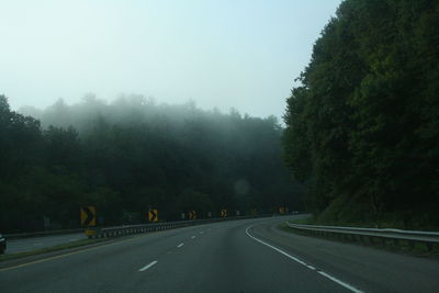 Street amidst trees against sky in foggy weather 