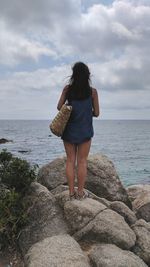 Rear view of young woman standing by sea against sky