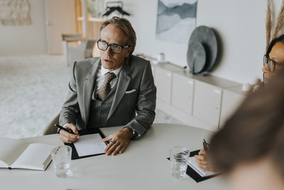 Mature businessman sitting by senior businesswoman at conference table in board room