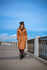 Beautiful woman in a cap and jacket posing while standing on the embankment