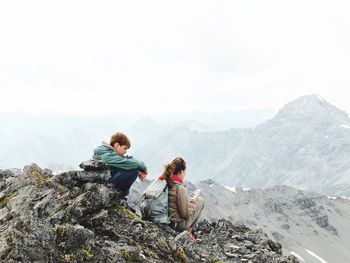 Friends sitting on mountain against sky