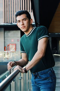 Portrait of young man standing against railing