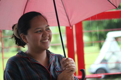 Smiling woman holding umbrella during rainy season