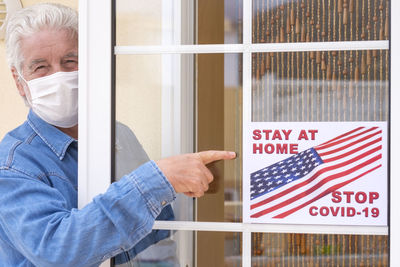 Portrait of man wearing mask showing sign at entrance