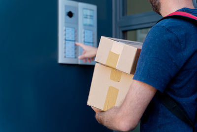Midsection of delivery person holding parcel ringing doorbell