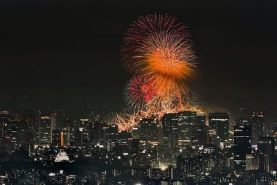 Firework display over cityscape against clear sky at night