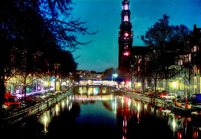 Illuminated bridge over river by buildings in city at night