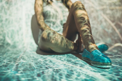 Low section of woman sitting on swimming pool