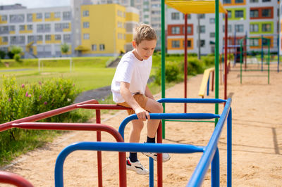 The boy does sports on horizontal bars of different colors