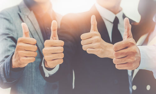 Midsection of business people showing thumbs up
