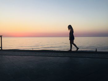 Side view of silhouette woman walking on retaining wall against sea during sunset