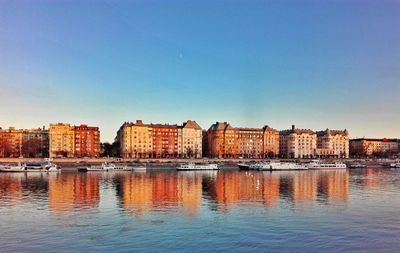 Cityscape by sea against clear blue sky