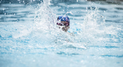 Girl splashing water while swimming in pool