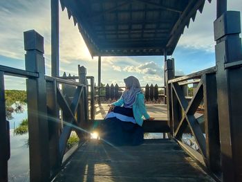 Woman wearing hijab sitting on footbridge