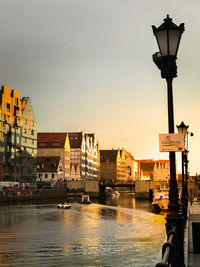 Street light by river against buildings in city at dusk