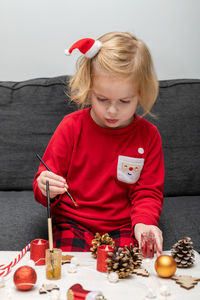 Little child wearing christmas holiday pajamas, doing crafts christmas tree decorations.