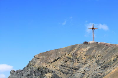 Low angle view of cross on mountain against blue sky