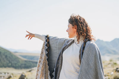 Brunette young woman traveler in poncho from back on beautiful view of mountains