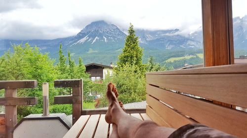 Man sitting on wooden bench against sky