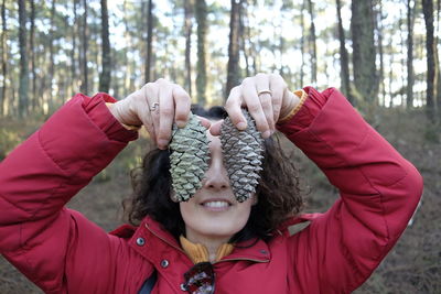 Close-up woman holding pine cone against trees