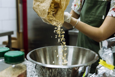 Female baker pouring ingredient in mixing bowl at bakery kitchen