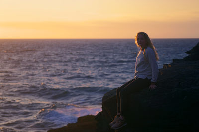 Young woman sitting by sea on rock during sunset