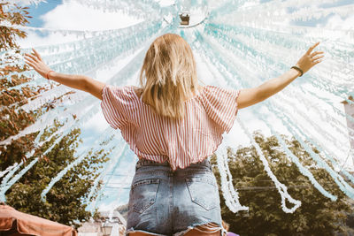 Back view of blonde woman with open arms enjoying a festival