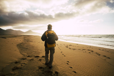 Rear view of backpacker walking on sand at beach during sunset