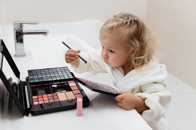 Toddler girl doing herself makeup with mama's cosmetics pretending grownup. applying eyeshadows