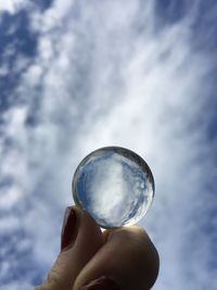 Close-up of hand holding crystal ball against sky