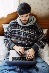High angle view of young man using laptop while relaxing on bed at home