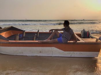 Woman sitting on boat at beach against sky