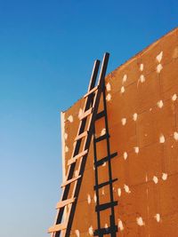 Low angle view of crane against building against clear blue sky