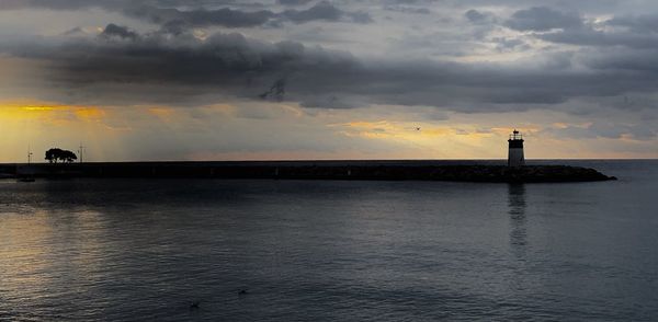 Silhouette lighthouse by sea against sky during sunset