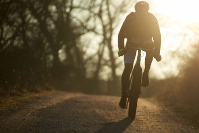 Silhouette woman riding bicycle on footpath against sky during sunset