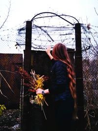 Woman standing by fence against sky