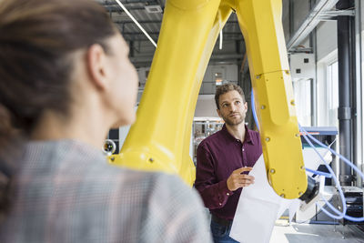 Businessman and woman having a meeting in front of industrial robots in a high tech company